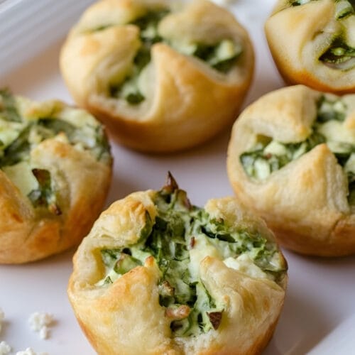 Freshly baked golden brown spinach and cheese puffs on a ceramic plate, showcasing the flaky puff pastry texture