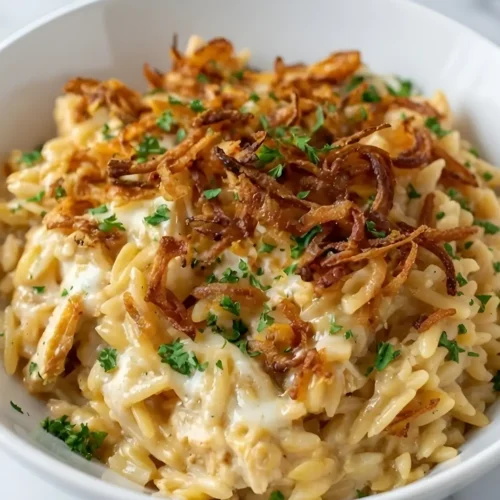 Close-up of creamy French Onion Chicken Orzo Casserole topped with crispy fried onions in a white bowl.