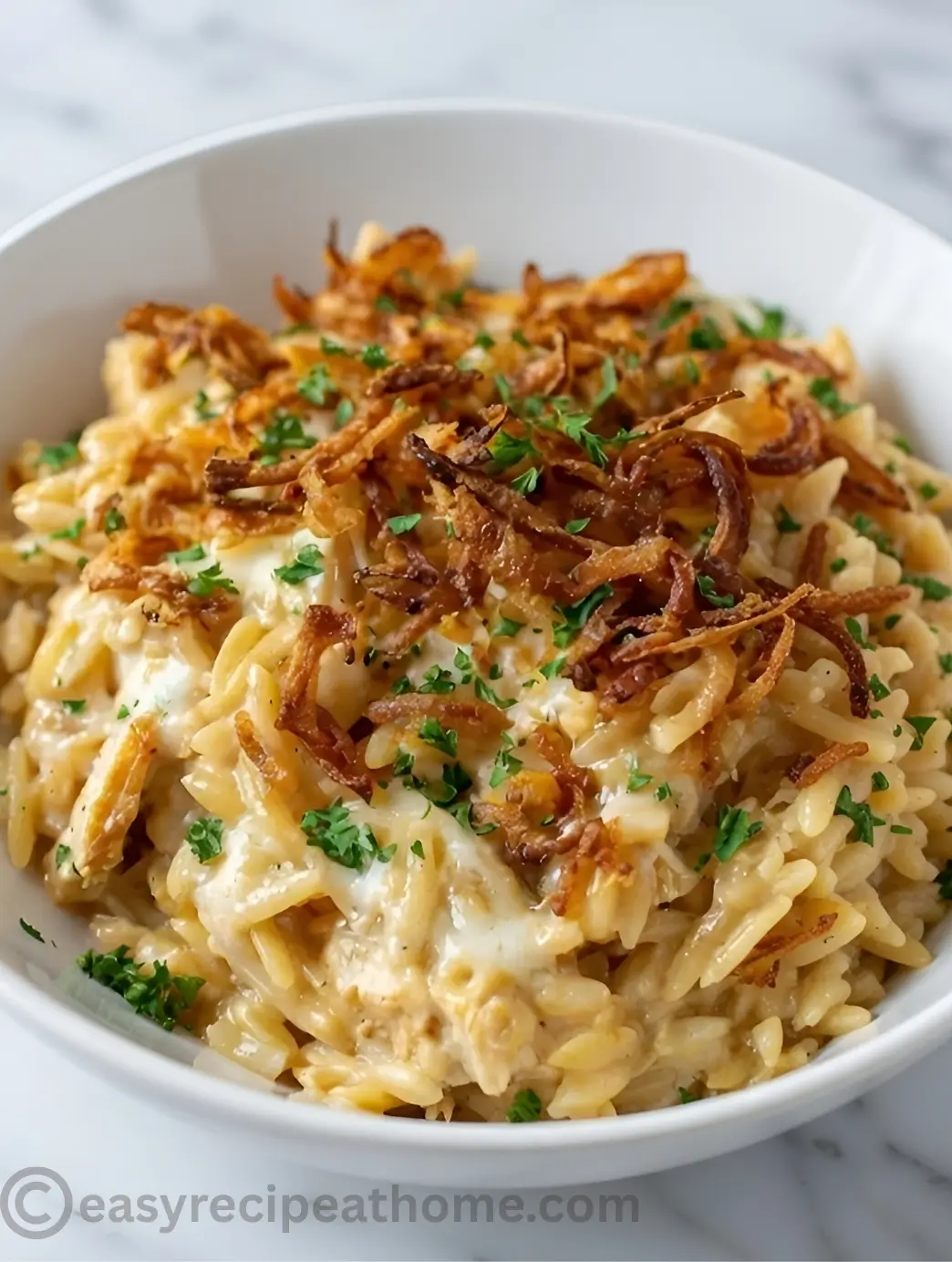 Close-up of creamy French Onion Chicken Orzo Casserole topped with crispy fried onions in a white bowl.