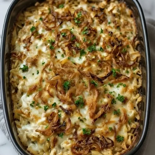 Close-up of creamy French Onion Chicken Orzo Casserole topped with crispy fried onions in a black baking dish