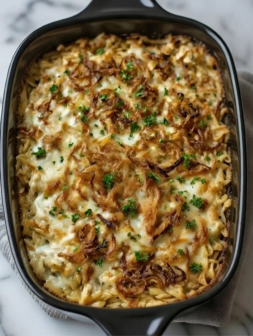 Close-up of creamy French Onion Chicken Orzo Casserole topped with crispy fried onions in a black baking dish