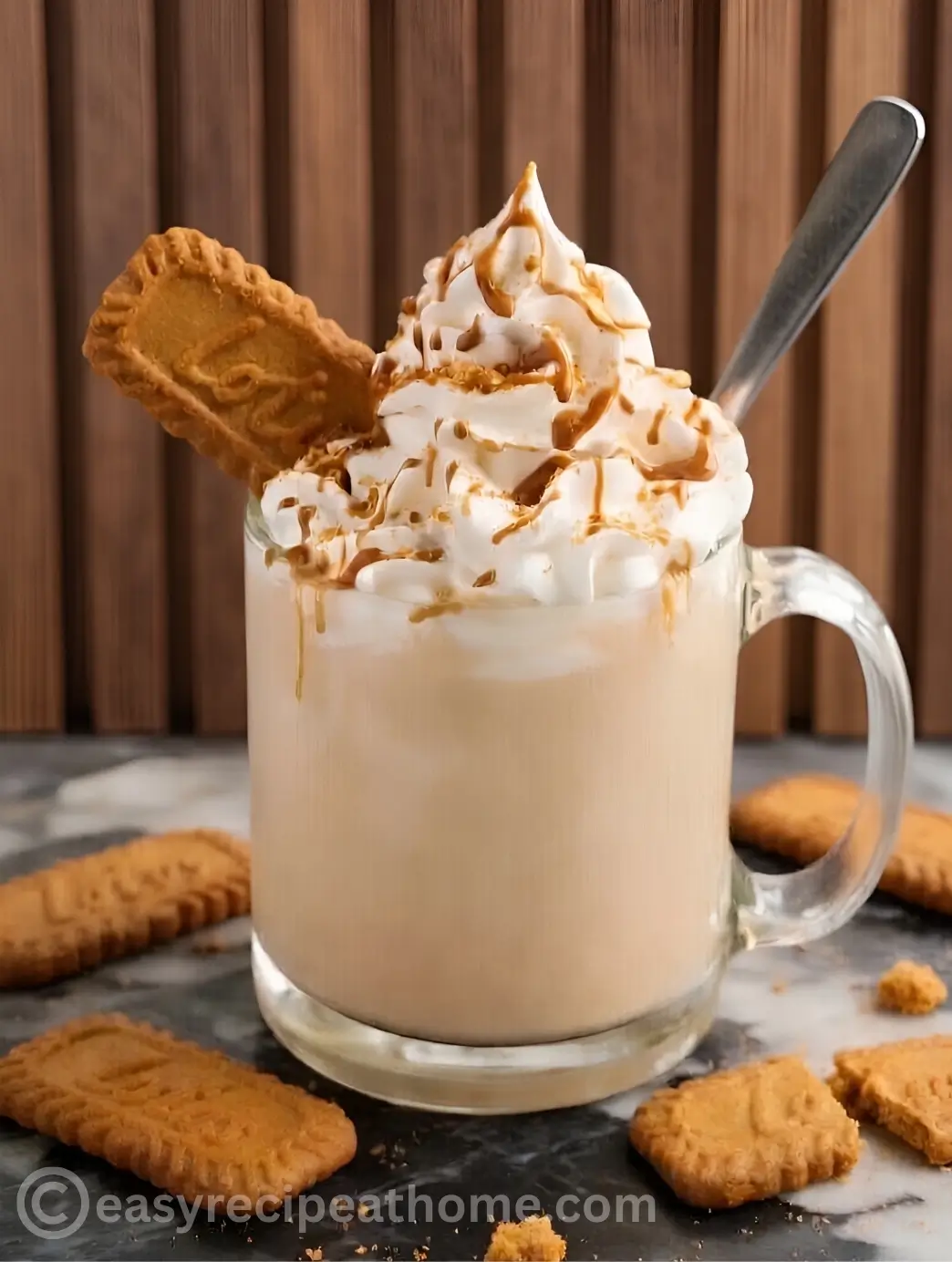 A glass mug filled with a hot, creamy Biscoff Cookie Butter Latte dunkin, beautifully topped with fluffy whipped cream, melted speculoos cookie butter drizzle, and crushed Lotus biscuits.