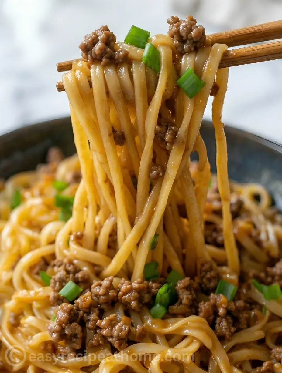 Savory Mongolian noodles with ground beef stir-fry and green scallions being held by chopsticks.
