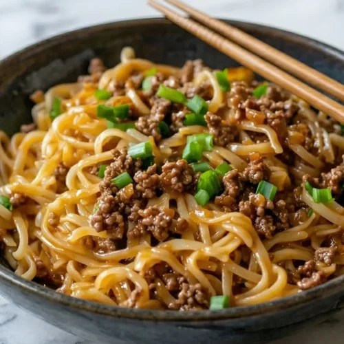 A close-up bowl of saucy Mongolian ground beef noodles garnished with green onions