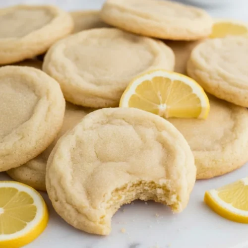 Overhead view of lemon sugar cookies on parchment paper, with one broken in half to show the soft, moist interior texture