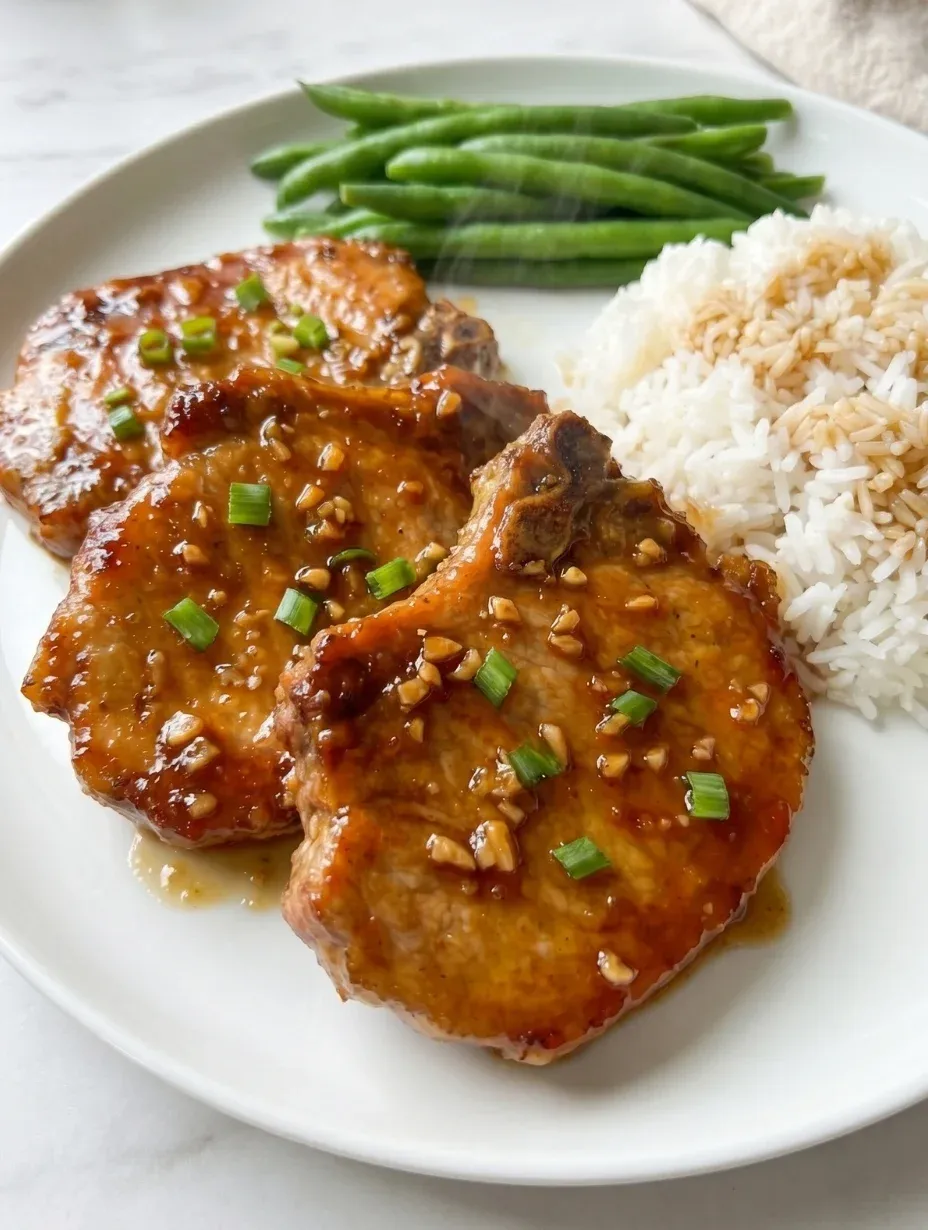 Sticky honey garlic pork chops resting on a bed of fluffy white rice.