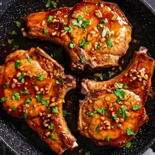 Glistening honey garlic pork chops garnished with fresh parsley in a skillet.