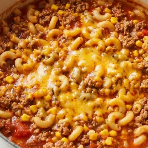 A large heavy pan filled with cheesy one-pot chili mac featuring ground beef, tender macaroni noodles, and melted cheddar cheese in a rich tomato broth.
