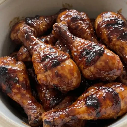 A heavy ceramic slow cooker filled with bone-in crock pot chicken drumsticks heavily coated in a thick, dark molasses barbecue sauce and dry spice rub.