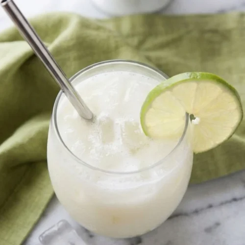 Angled overhead view showing the icy mixture and the lime wheel garnish on a glass of fresh Brazilian lemonade, part of a step-by-step Brazilian lemonade recipe guide.
