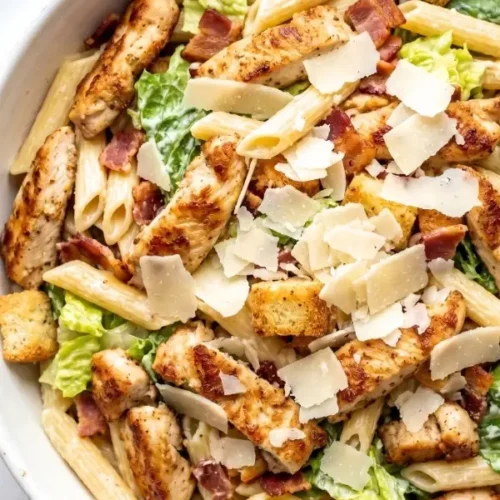 Close up of chicken Caesar pasta salad with golden pan fried chicken strips, crispy bacon, penne pasta and crunchy garlic croutons tossed in homemade Caesar dressing