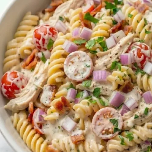 Creamy chicken bacon ranch pasta salad with rotini pasta, crispy bacon, cherry tomatoes, shredded rotisserie chicken and homemade ranch dressing in a white serving bowl