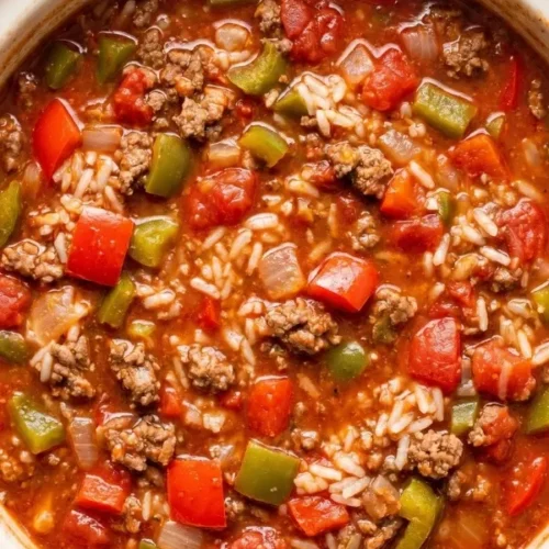 A massive ceramic slow cooker bowl completely filled with fiercely bubbling, wildly rich stuffed pepper soup heavily loaded with aggressively browned ground beef and vibrant chopped bell peppers in a deeply dark tomato broth