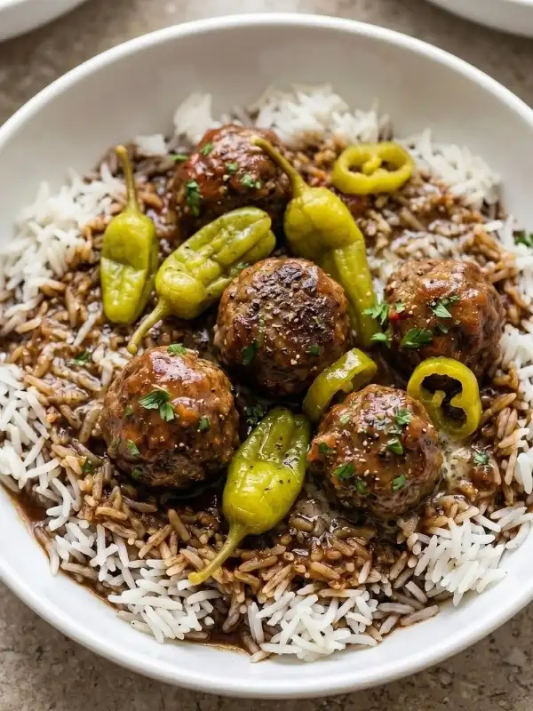 Mississippi meatballs aggressively covered in a deeply dark, bubbling au jus butter gravy and violently bright pepperoncini peppers served with wildly fluffy white rice in a white plate