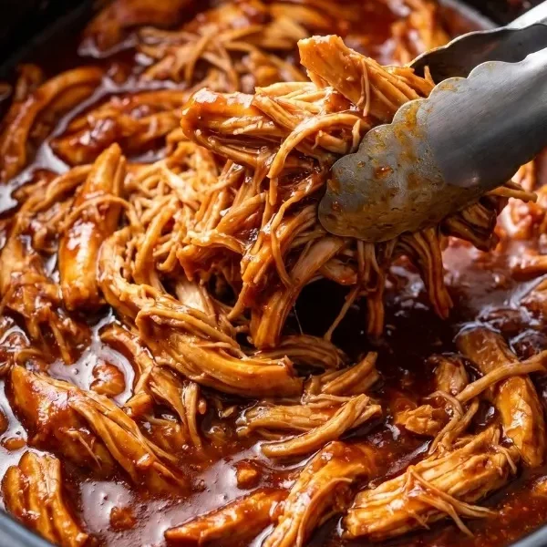 A massive ceramic slow cooker bowl completely filled with fiercely bubbling, wildly sticky shredded Dr. Pepper chicken heavily coated in a deeply dark, rich barbecue sauce glaze.