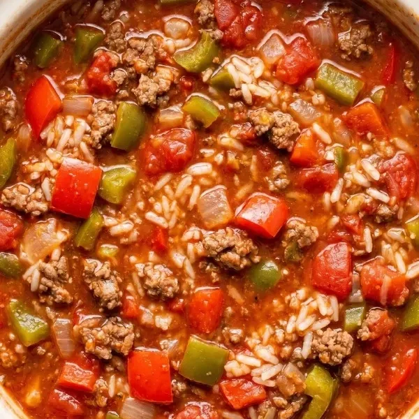 A massive ceramic slow cooker bowl completely filled with fiercely bubbling, wildly rich stuffed pepper soup heavily loaded with aggressively browned ground beef and vibrant chopped bell peppers in a deeply dark tomato broth