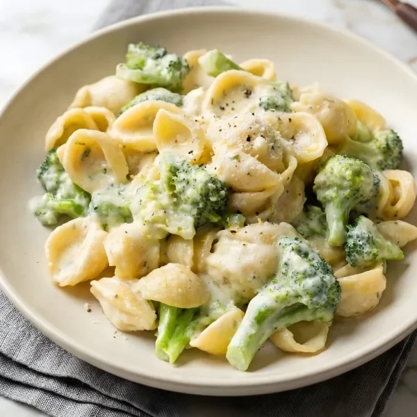 A plate of creamy broccoli pasta with shell noodles and fresh broccoli florets, topped with cracked black pepper